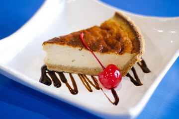 Pastel de queso con cereza sobre mesa azul 