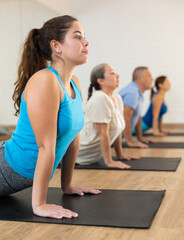 Fototapeta premium People of different ages performing cobra exercise during group Pilates workout. Active lifestyle and wellness concept
