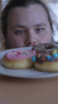 Overweight Person wanting to eat sugar food on plate. One Young fat man in diet fasting from junk food. Donut closeup in front of fat guy. Weight loss concept. Vertical Video