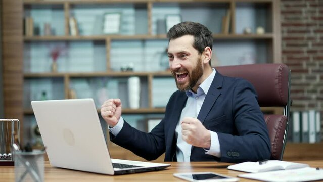 Overjoyed business man investor extremely happy after read email message on laptop at modern workplace Excited entrepreneur look at screen and pleased rejoices received great news on computer indoors