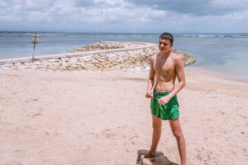 Young pretty muscular caucasian men smiling and looking down at someone on sand beach in front of sea, close up photo at Sanur beach Bali