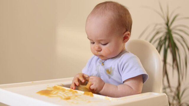 a cute kid in a yellow bodysuit is sitting in the kitchen with cans of baby food. The first complementary feeding of the child. Baby purees. High quality photo