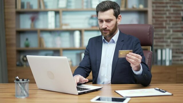 Smiling business man entrepreneur paying with credit card on laptop computer at the office workplace Happy customer employer do payments online shopping in internet store and receive cashback Easy pay