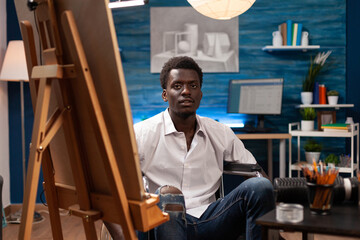 Male artist with spinal cord injury working in home art studio. African american professional...