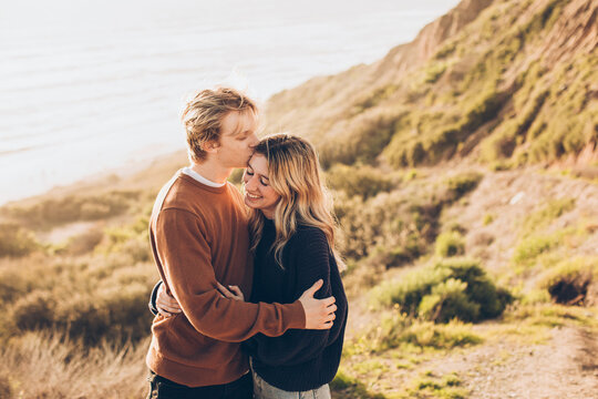 Couple Embracing At The Beach With Him Kissing Her On The Forehead