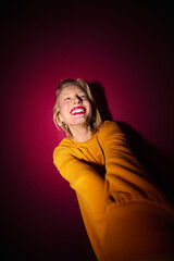 A happy young blond woman is laughing while standing in front of the magenta background. Viva magenta.