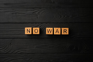 Wooden light yellow cubes with letters form the word War on a black wooden table. Dark background, flat lay, top view.