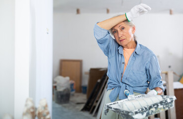 Portrait of an elderly tired female house painter in a renovated room