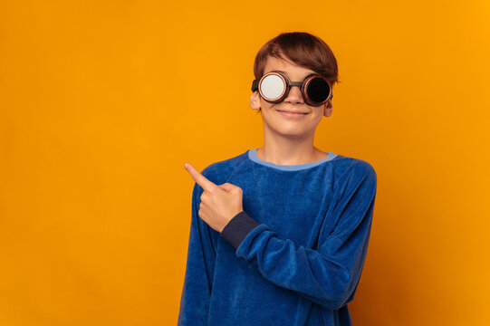 Smiling teen boy is pointing aside at copy space while wearing pilot glasses.
