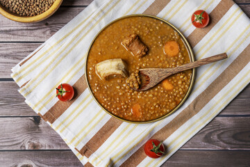 Traditional Spanish lentil stew with chorizo, bacon, vegetables with a wooden spoon on a kitchen towel