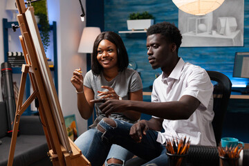 Art teacher showing new drawing technique to african american female student in home crafts studio....