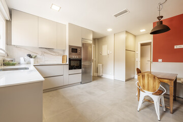 Open kitchen with stone countertop, sink and ceramic hob, cabinet with large drawers without handles, dining area with wooden table and large stoneware floor