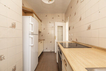 Kitchen with light wood cabinets with wood pulls, wood-look countertops, black and white appliances, and wood-colored trim