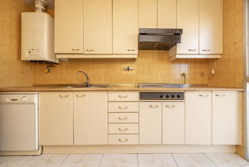 Frontal image of a kitchen with furniture with doors and drawers in cream-colored wood and light brown stoneware tiles