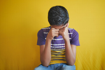 sad teenage boy covering his face sitting on sofa 