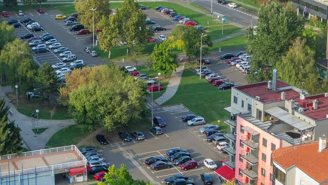 Cars moving on parking lot timelapse with green trees, lawn and residential buildings. Top view from skyscraper rooftop. Croatia, Zagreb