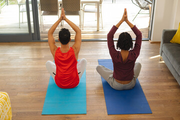 Rear view of diverse gay male couple practicing yoga and meditating together at home