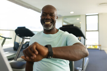 African american senior man using a smartwatch while sitting on stationary bike at the gym