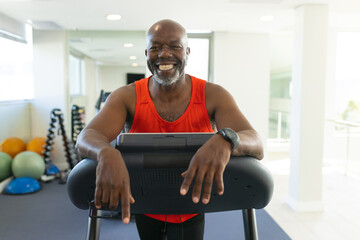 Portrait of african american senior man smiling while standing on the treadmill at the gym