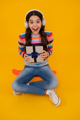 Amazed teenager. Child teen girl 12-14 years old with gift on yellow isolated background. Birthday, holiday present concept. Excited teen girl.