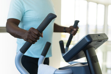 Mid section of african american senior man using elliptical machine at the gym