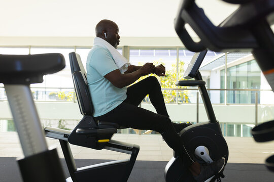 African american senior man using a smartwatch while training on stationary bike at the gym