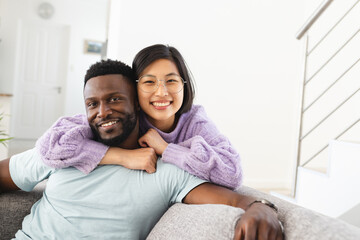 Portrait of happy diverse couple sitting on sofa and embracing