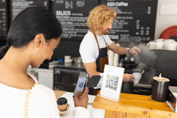 Happy diverse male barista and woman scanning qr code with smartphone in cafe