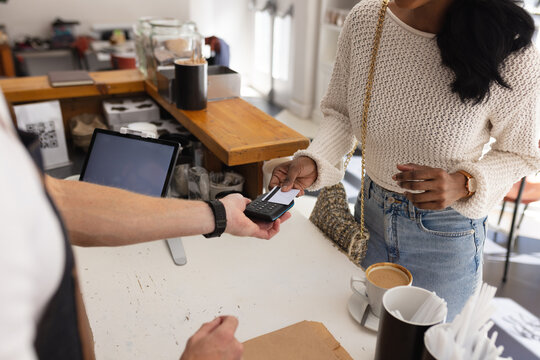 Diverse male barista and woman paying with credit card in cafe