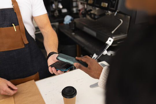 Diverse male barista and woman paying with smartphone in cafe