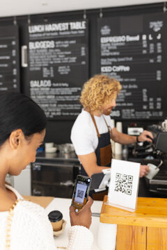 Happy diverse male barista and woman scanning qr code with smartphone in cafe
