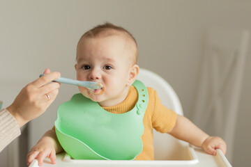 baby 1 year old eats baby food from a spoon sitting at the table, the first complementary foods and healthy food for small children.Close up