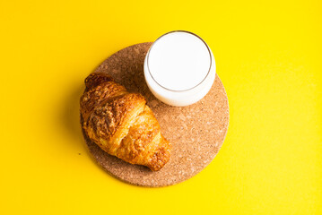 Breakfast bread and a cup of milk on yellow and blue background