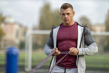 Athletic man in sportswear pumps his back muscles with an elastic band