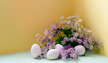 white chicken eggs lie near a bouquet of lilac flowers on a yellow front