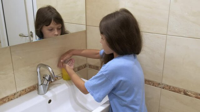 Childhood with clean hands. A young girl washes her hands with soap under running water in the bathroom.