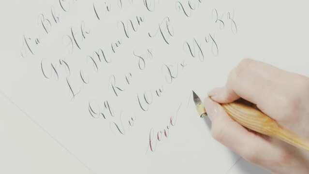 Close up of a a woman's hand writing the alphabet with cursive letters and using a fountain pen, calligraphy concept
