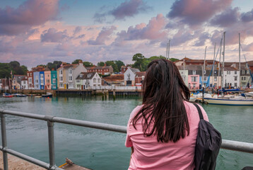Fototapeta na wymiar woman in focus enjoying the view of the bay with ships and boats of the seaside town Weymouth, England
