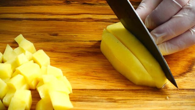 The cook cuts potatoes on a cutting board.