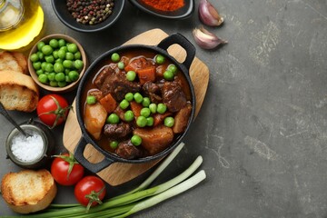 Delicious beef stew and ingredients on grey table, flat lay. Space for text