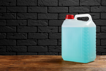 Plastic canister with blue liquid on wooden table against dark brick wall, space for text