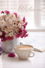 Welcome card. Cup of fresh coffee, open book and beautiful bouquet on white wooden table near window
