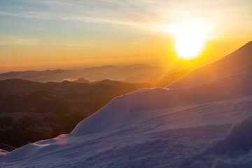 Yellow disc of sun at the sunrise in the snowy winter mountains