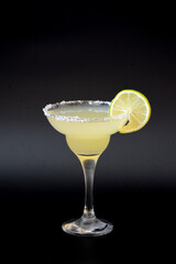 Margarita cocktail, a tall glass with a drink, sugar around the rim and a slice of lemon on a black background.