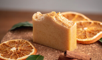 Piece of natural soap and slices of oranges, cinnamon and green leaves on the wooden background