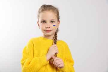 Little girl with drawing of Ukrainian flag on face against white background