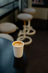 A hot latte coffee served in a paper cup on a black table at a coffee shop.
