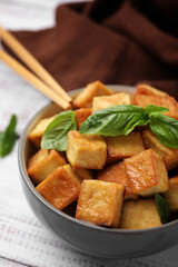 Bowl with delicious fried tofu and basil on white table