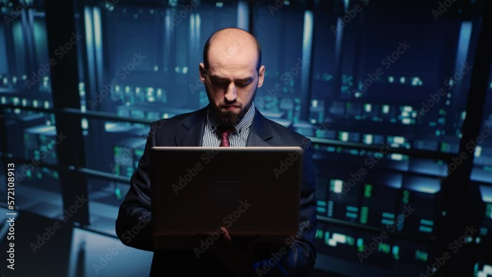Poster system engineer running hosting server diagnostics with laptop, standing in modern big data center s