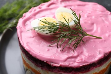 Herring under fur coat salad on black plate, closeup. Traditional Russian dish